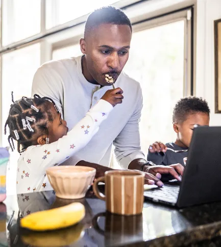Father cooking dinner for kids while working on his laptop