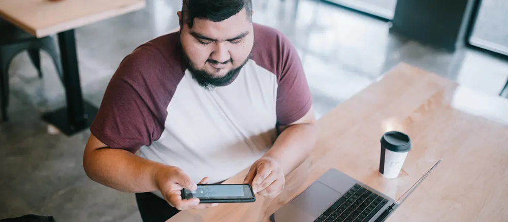 College age male sitting in a coffee shop on his phone